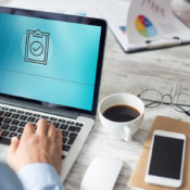 ISO 9001:2026: laptop con icona di checklist approvata su una scrivania con documenti e grafici