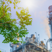 GHG Protocol e ISO 14064-1: fronde verdi davanti a un impianto industriale con camino in funzione